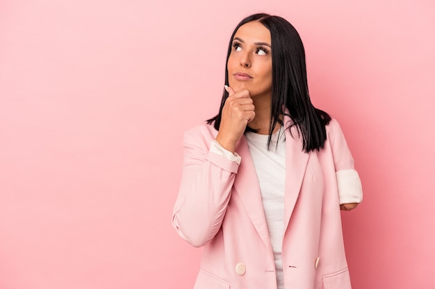 Jeune femme caucasienne avec un bras isolé sur fond rose regardant de côté avec une expression douteuse et sceptique.