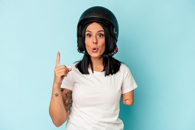 Jeune femme caucasienne avec un bras portant un casque de moto isolé sur fond bleu ayant une bonne idée, concept de créativité.