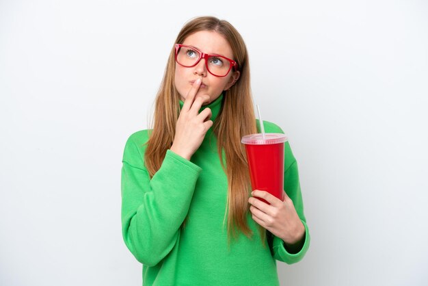 Jeune femme caucasienne buvant du soda isolé sur fond blanc ayant des doutes en levant les yeux