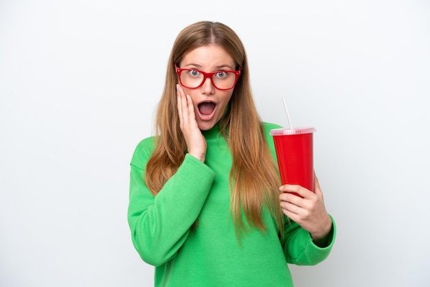 Jeune femme caucasienne buvant du soda isolé sur fond blanc avec une expression faciale surprise et choquée