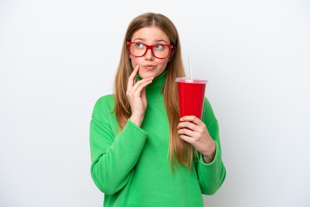 Jeune femme caucasienne buvant du soda isolé sur fond blanc en pensant à une idée tout en levant les yeux