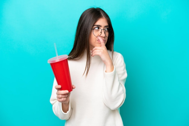 Jeune femme caucasienne buvant du soda isolé sur fond bleu ayant des doutes