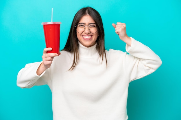 Jeune femme caucasienne buvant du soda isolé sur fond bleu faisant un geste fort