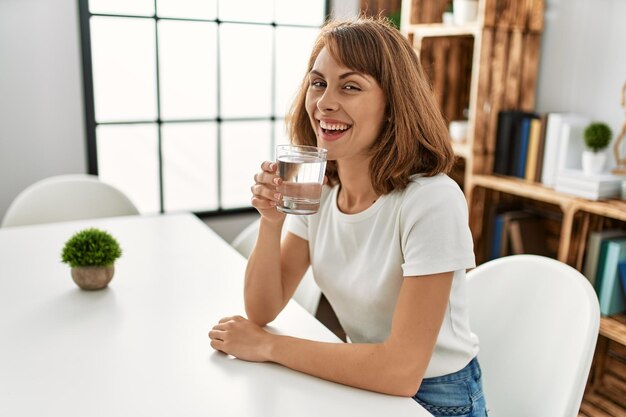 Jeune femme caucasienne buvant de l'eau assise sur une table à la maison