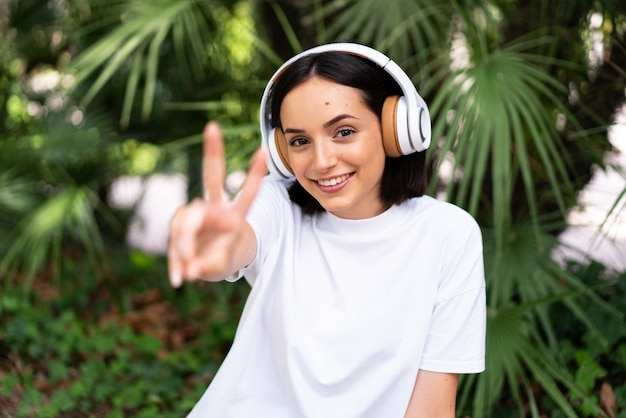 Jeune femme caucasienne avec un casque à l'extérieur souriant et montrant le signe de la victoire