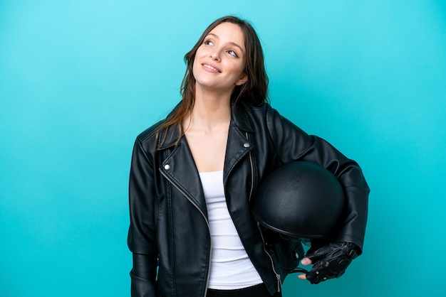 Jeune femme caucasienne avec un casque de moto isolé sur fond bleu pensant à une idée tout en levant les yeux