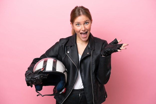 Jeune femme caucasienne avec un casque de moto isolé sur fond rose avec une expression faciale choquée