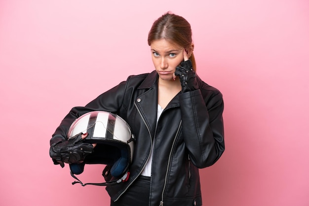 Jeune femme caucasienne avec un casque de moto isolé sur fond rose en pensant à une idée