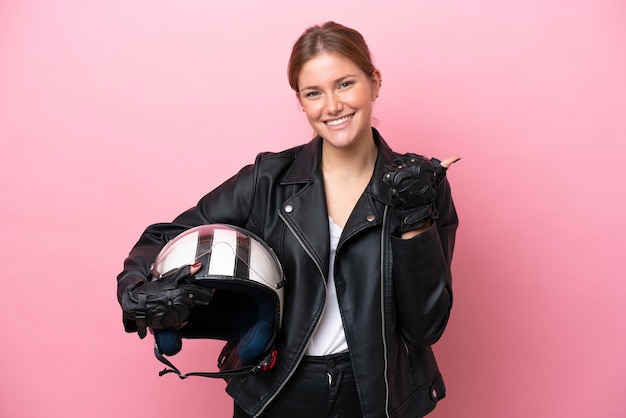 Jeune femme caucasienne avec un casque de moto isolé sur fond rose pointant vers le côté pour présenter un produit