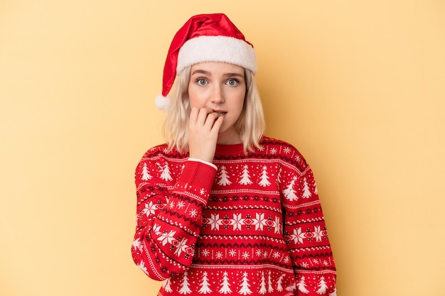 Jeune femme caucasienne célébrant Noël isolée sur fond jaune se rongeant les ongles, nerveuse et très anxieuse.