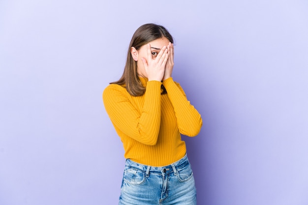 Jeune femme caucasienne cligner des yeux à travers les doigts effrayés et nerveux.