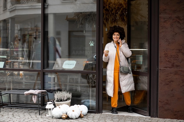 Jeune femme caucasienne. Coiffure Afro. Vêtements de sport décontractés. Walking European Street, tenant une tasse de café ou de thé. La vie en ville, le style de la rue