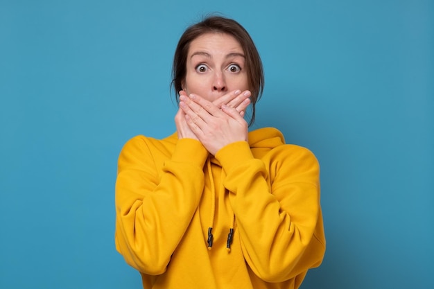 Jeune femme caucasienne couvrant avec la main sa bouche, isolée sur fond bleu