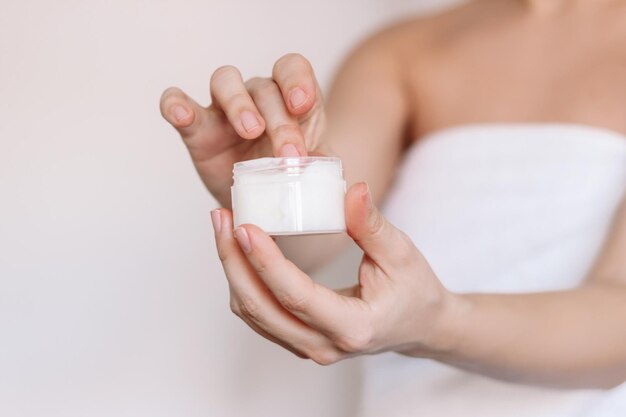 Photo une jeune femme caucasienne dans une serviette blanche après une douche prenant de la crème hydratante avec son doigt