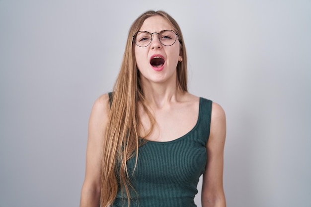 Jeune femme caucasienne debout sur fond blanc en colère et folle criant frustré et furieux, criant de colère. rage et concept agressif.