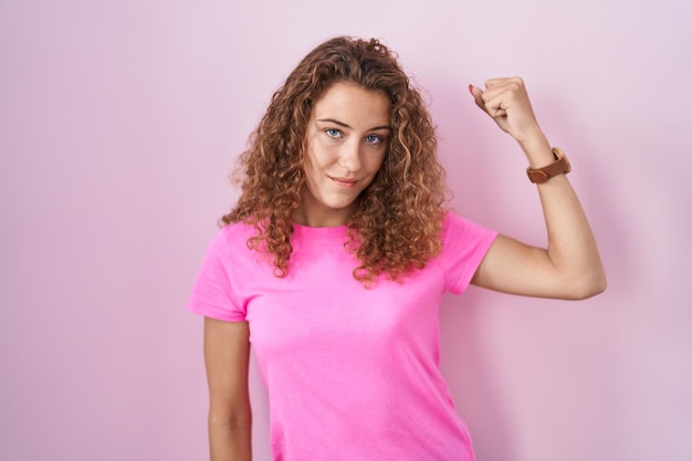 Jeune femme caucasienne debout sur fond rose personne forte montrant le muscle du bras confiant et fier du pouvoir