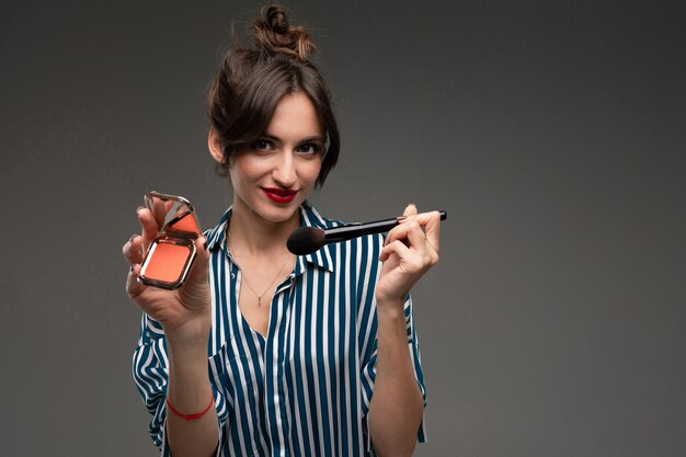 Une jeune femme caucasienne détient des pinceaux de maquillage isolés sur fond gris