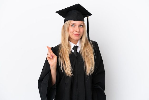 Jeune femme caucasienne diplômée universitaire isolée sur fond blanc avec les doigts croisés et souhaitant le meilleur