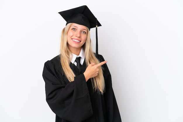 Jeune femme caucasienne diplômée universitaire isolée sur fond blanc pointant le doigt sur le côté