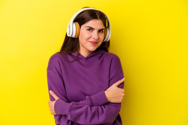 Jeune femme caucasienne écoutant de la musique avec des écouteurs isolés sur fond rose qui se sent confiante, croisant les bras avec détermination.