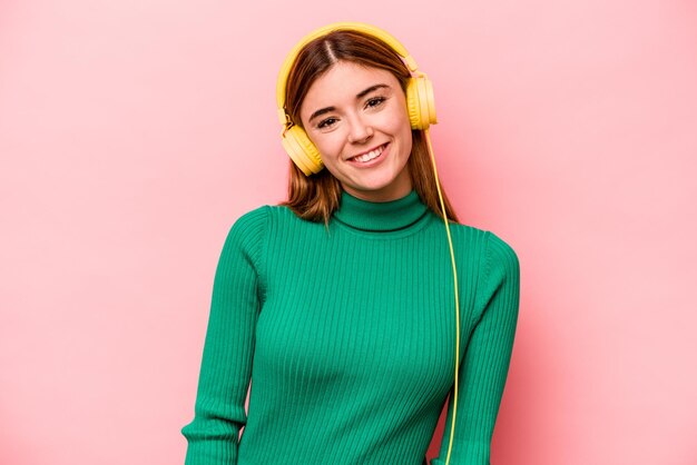 Jeune femme caucasienne écoutant de la musique isolée sur fond rose heureux souriant et joyeux