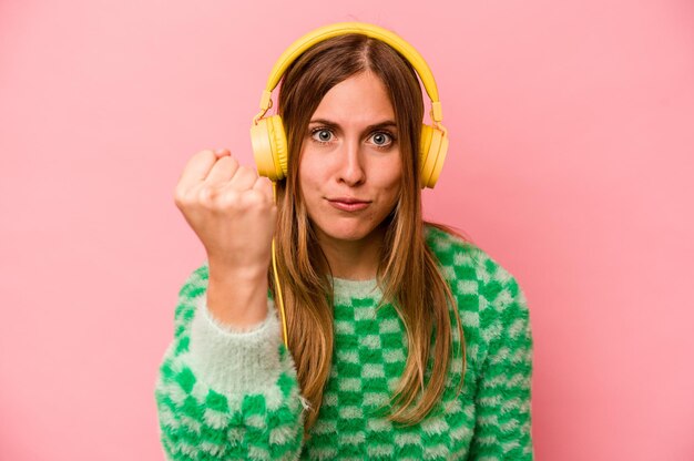 Jeune femme caucasienne écoutant de la musique isolée sur fond rose montrant le poing à la caméra expression faciale agressive