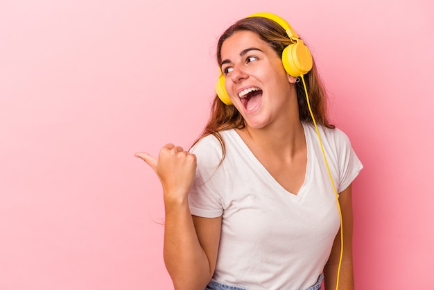 Jeune femme caucasienne écoutant de la musique isolée sur des points de fond rose avec le pouce loin, riant et insouciant.