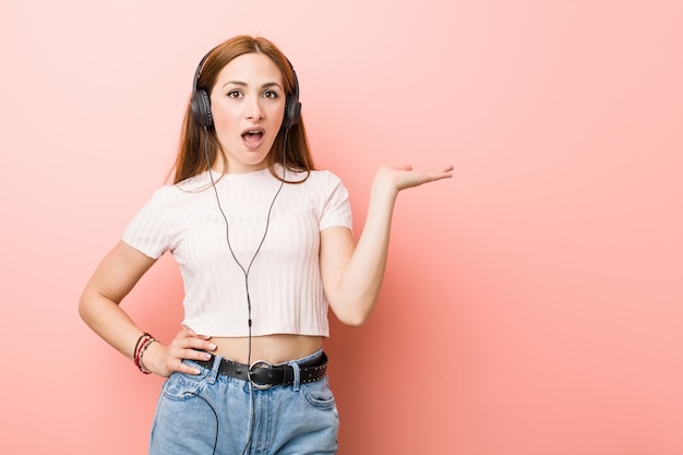 Jeune femme caucasienne écouter de la musique impressionné maintenant espace copie sur la paume.