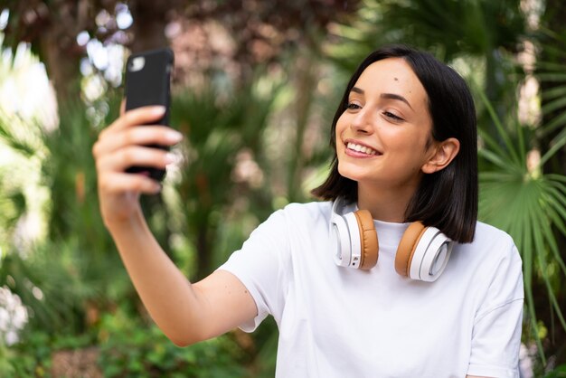 Jeune femme caucasienne avec des écouteurs à l'extérieur faisant un selfie