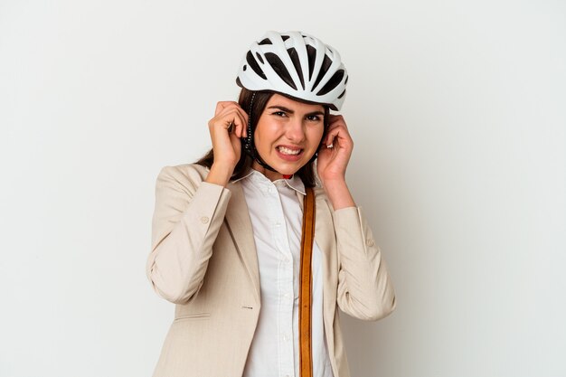 Jeune femme caucasienne, faire du vélo pour travailler isolé sur fond blanc couvrant les oreilles avec les mains.