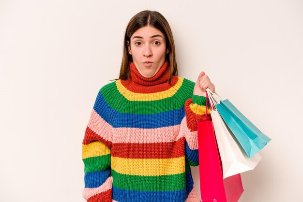 Jeune femme caucasienne faisant du shopping isolé sur fond blanc hausse les épaules et ouvre les yeux confus