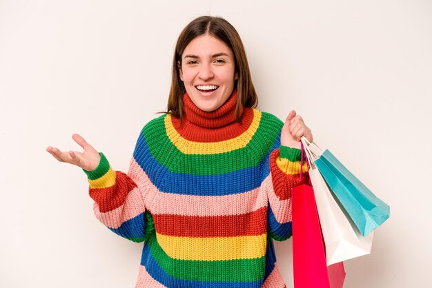 Jeune femme caucasienne faisant du shopping isolée sur fond blanc recevant une agréable surprise excitée et levant les mains