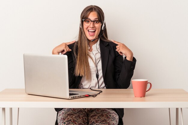 Jeune femme caucasienne faisant du télétravail isolé sur fond blanc surpris en pointant du doigt, souriant largement.