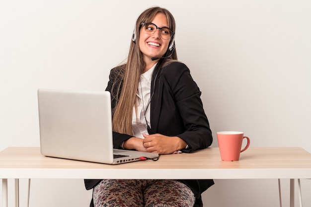 Jeune femme caucasienne faisant du télétravail isolée sur fond blanc regarde de côté souriante, gaie et agréable.