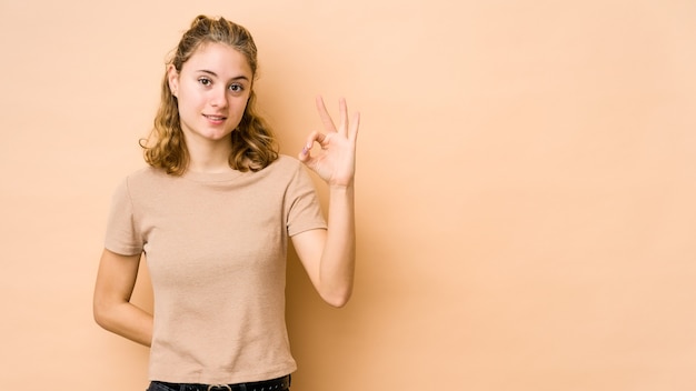 Jeune femme caucasienne fait un clin d'œil et tient un bon geste avec la main.