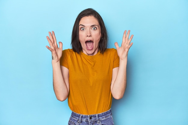 Jeune femme caucasienne sur fond bleu célébrant une victoire ou un succès, il est surpris et choqué