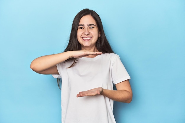 Jeune femme caucasienne sur fond bleu tenant quelque chose avec les deux mains présentation du produit