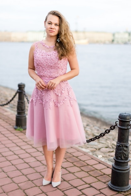 Photo jeune femme caucasienne frisée en robe rose rose au-dessous de ses genoux sur le talus.