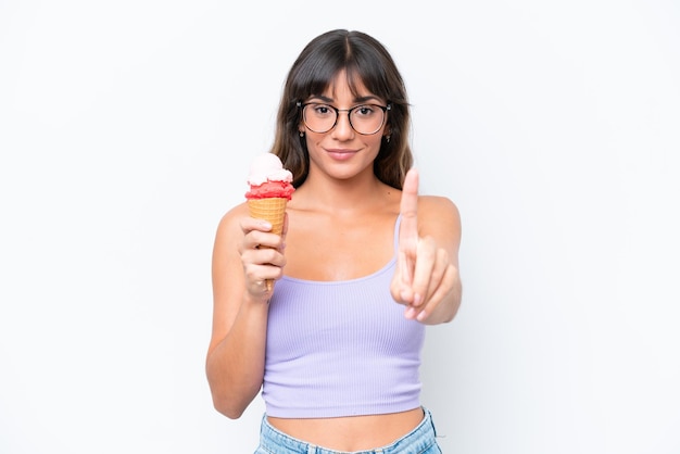 Jeune femme caucasienne avec une glace au cornet sur fond blanc isolé montrant et levant un doigt