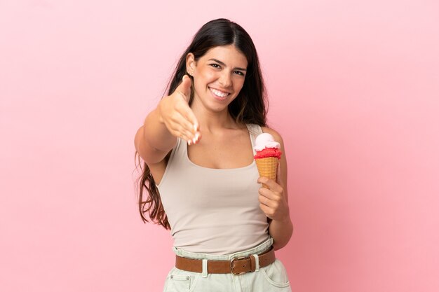 Jeune femme caucasienne avec une glace au cornet isolée sur fond rose se serrant la main pour conclure une bonne affaire