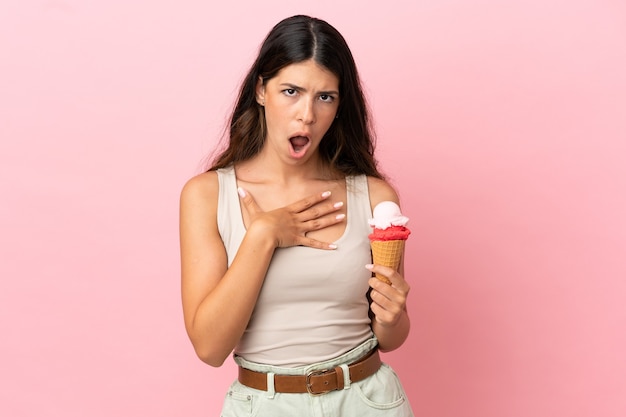 Jeune femme caucasienne avec une glace au cornet isolée sur fond rose surprise et choquée en regardant à droite