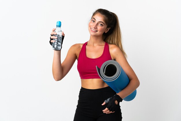 Jeune femme caucasienne isolée sur blanc avec bouteille d'eau de sport et avec un tapis