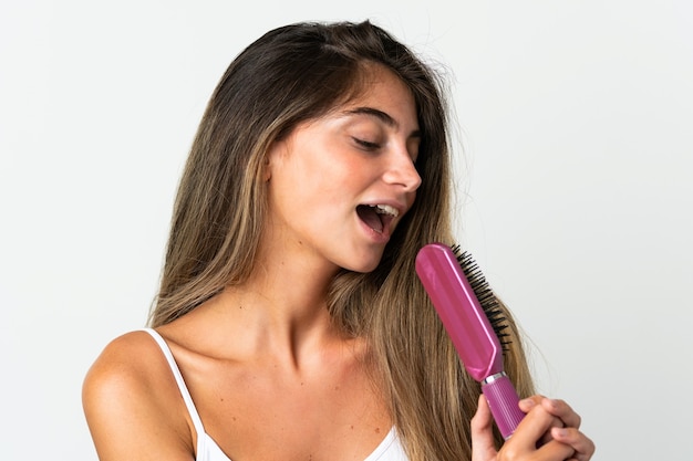 Jeune femme caucasienne isolée sur blanc avec peigne à cheveux et chant