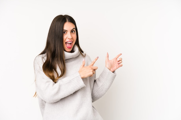 Jeune femme caucasienne isolée sur un blanc pointant avec l'index vers un espace de copie, exprimant l'excitation et le désir.