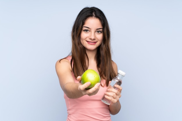 Jeune femme caucasienne isolée sur bleu avec une pomme et avec une bouteille d'eau