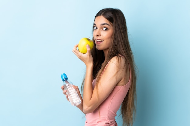 Jeune femme caucasienne isolée sur bleu avec une pomme et avec une bouteille d'eau