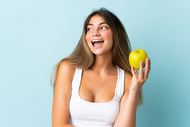 Jeune femme caucasienne isolée sur bleu avec une pomme et heureux