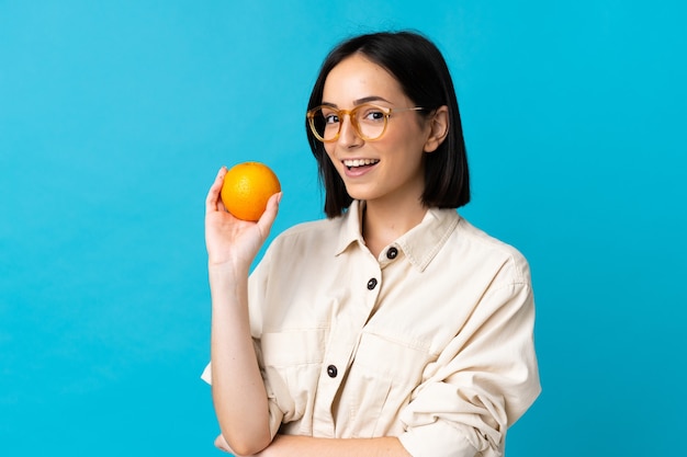 Jeune femme caucasienne isolée sur bleu tenant une orange