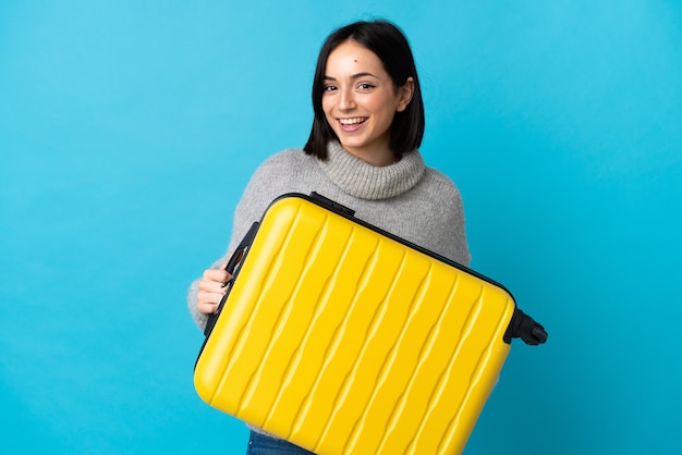 Jeune femme caucasienne isolée sur bleu en vacances avec valise de voyage