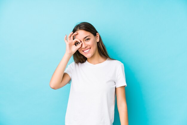 Jeune femme caucasienne isolée excité en gardant le geste ok sur les yeux.